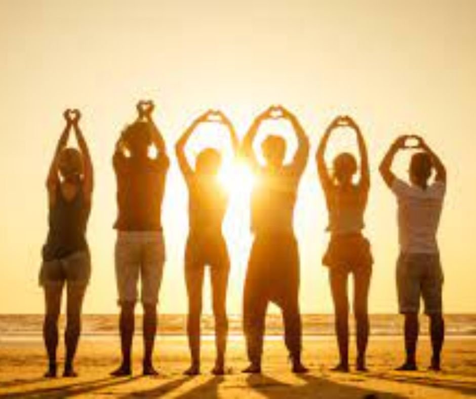 Shadow of six people forming heart shapes with their hands on a beach at sunset.