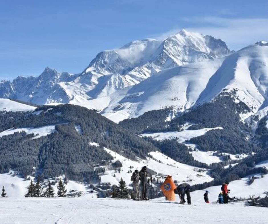 Skiers on a snowy mountain slope with towering peaks in the background.