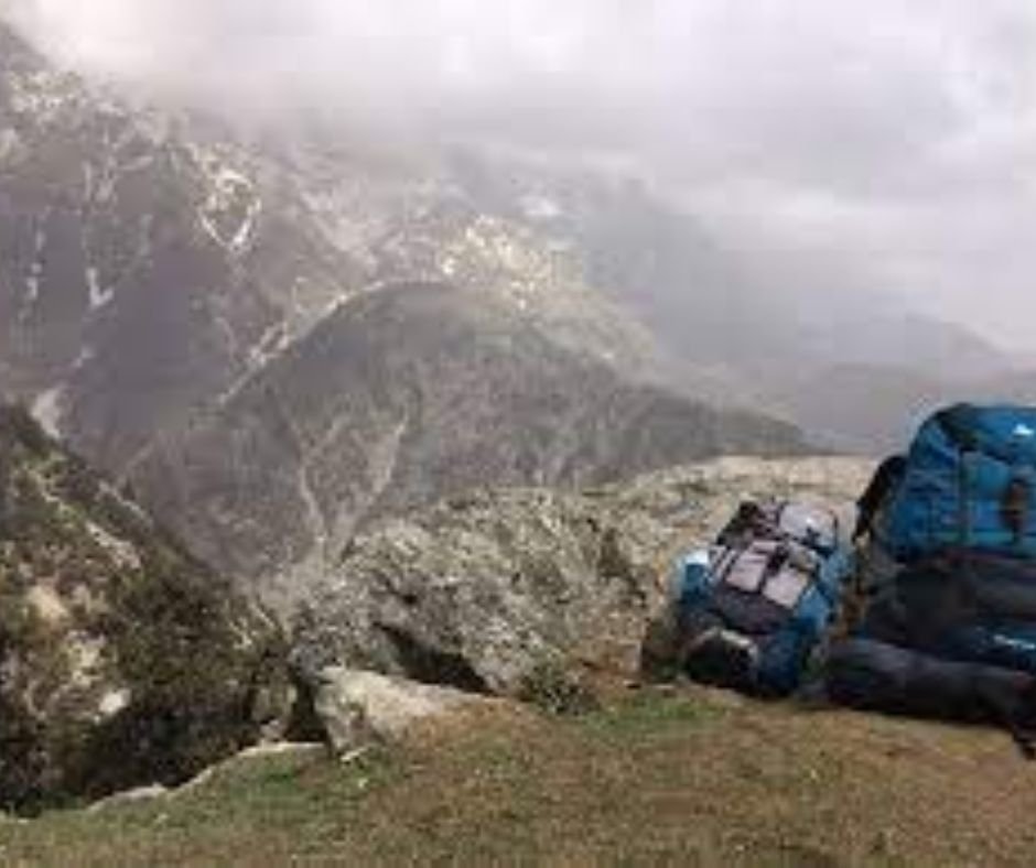 Backpacks on a mountain ledge overlooking a misty valley.